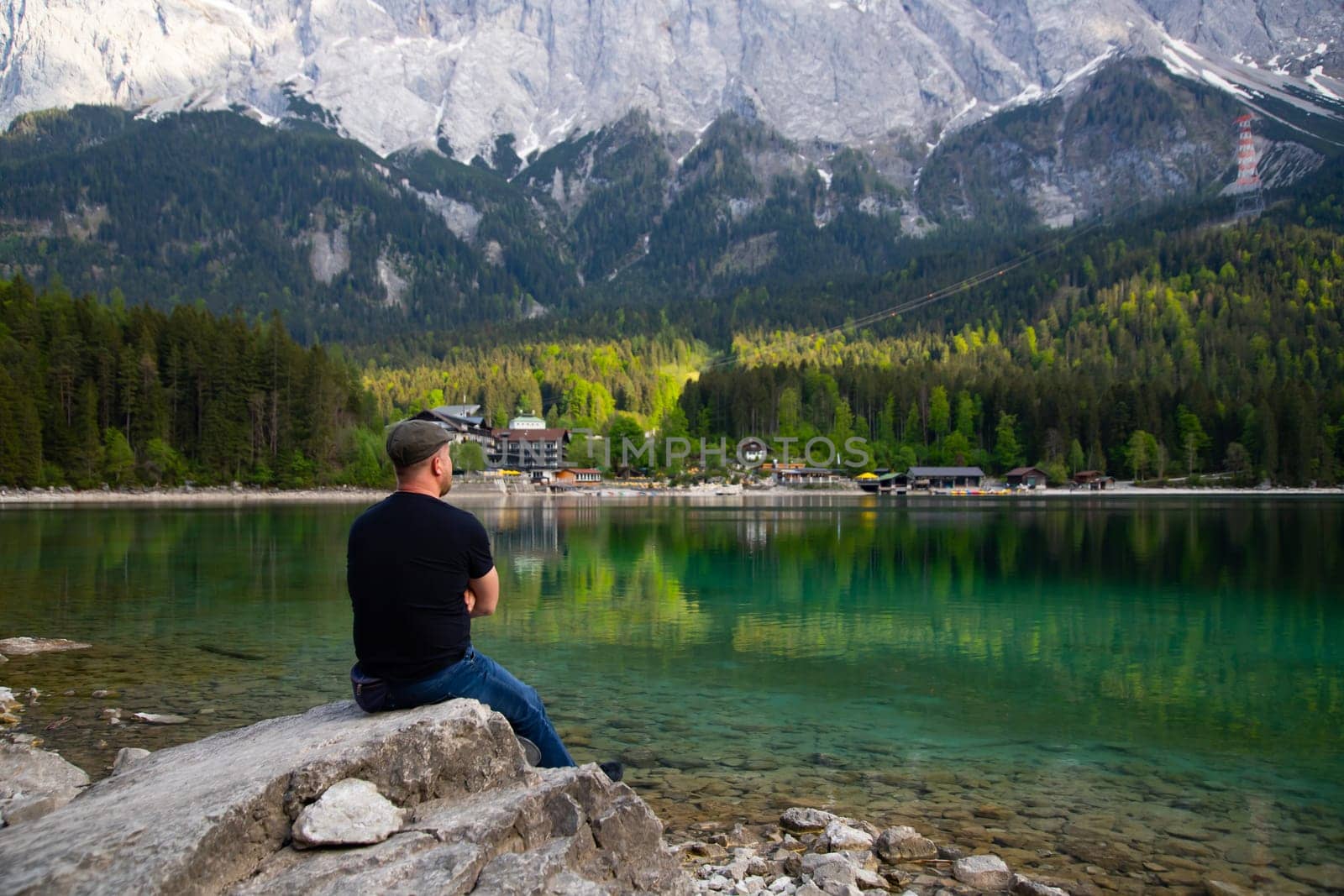 Tourist sitting on a rock and watching a beautiful view over lake Eibsee in the Bavarian Alps. Famous touristic destination in Europe