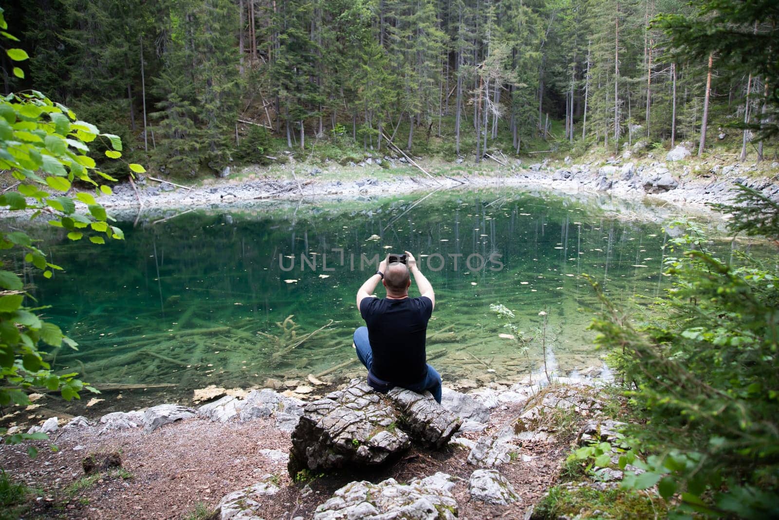 Tourist sitting on a rock and watching a beautiful view over lake Eibsee in the Bavarian Alps. Famous touristic destination in Europe
