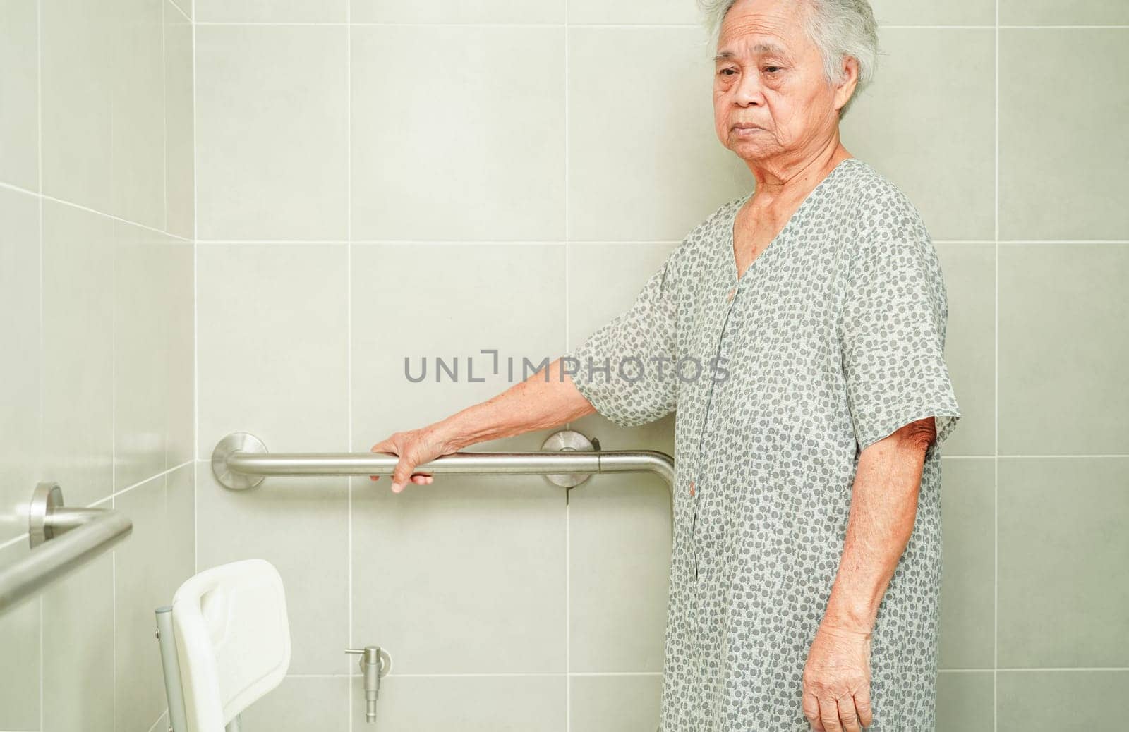Asian elderly old woman patient use toilet support rail in bathroom, handrail safety grab bar, security in nursing hospital.