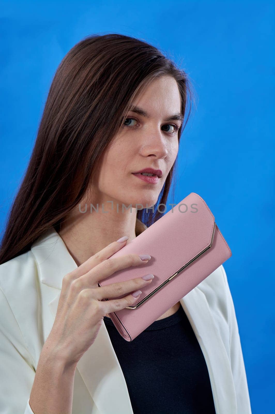 A beautiful young woman is holding a pink purse on a blue background, copy space. High quality photo