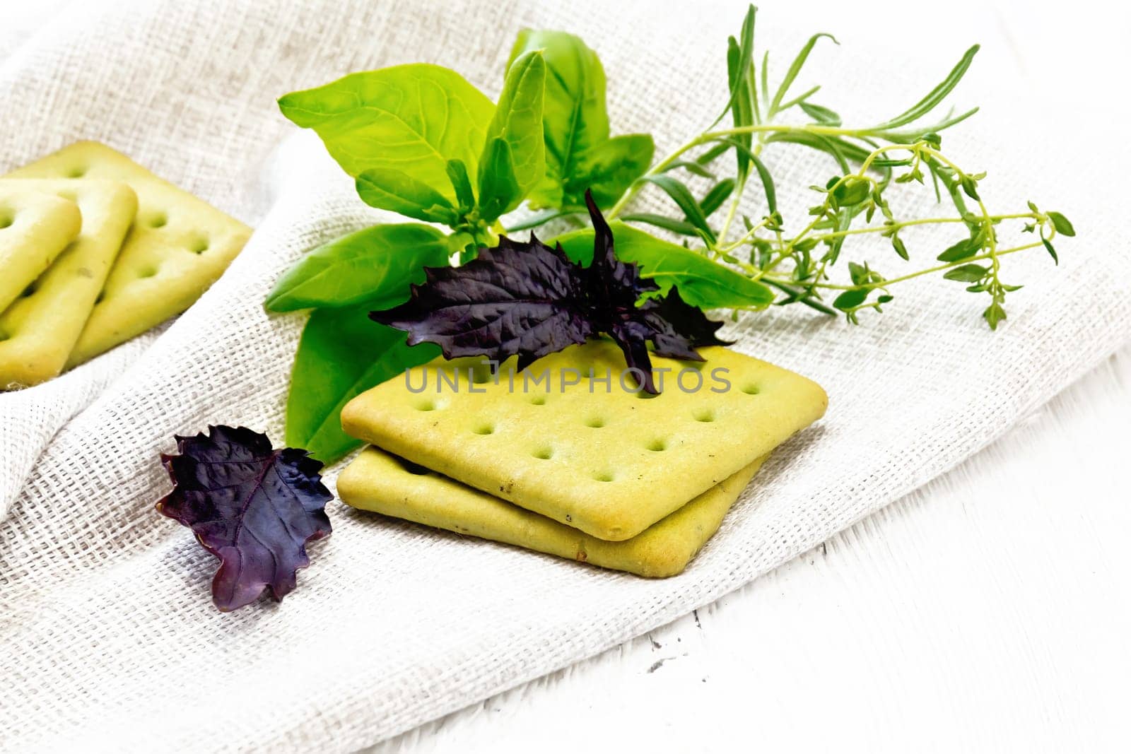 Dry biscuits with spinach, purple basil. rosemary and thyme on a towel on a light wooden board background