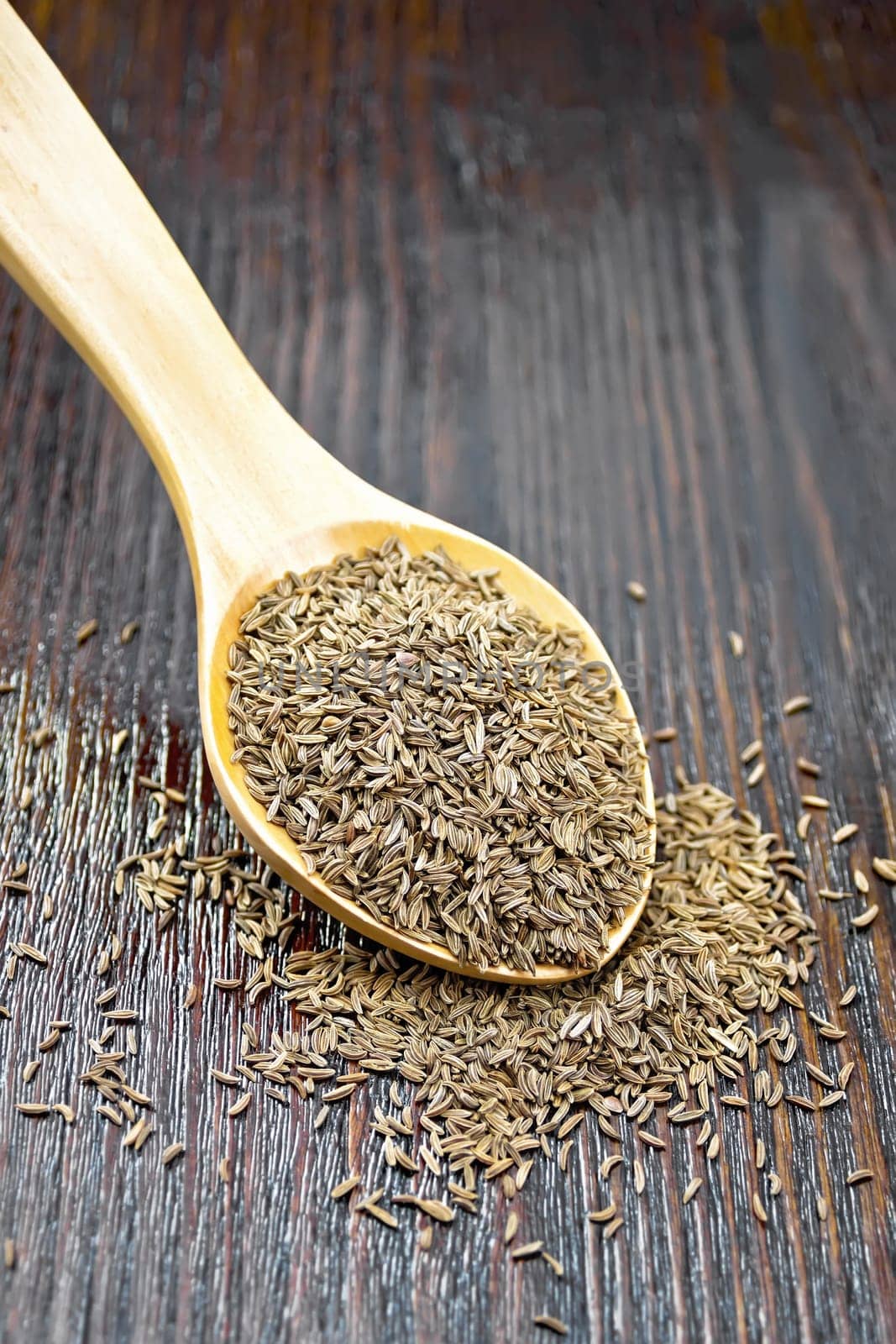 Cumin seeds in a spoon on dark wooden board background