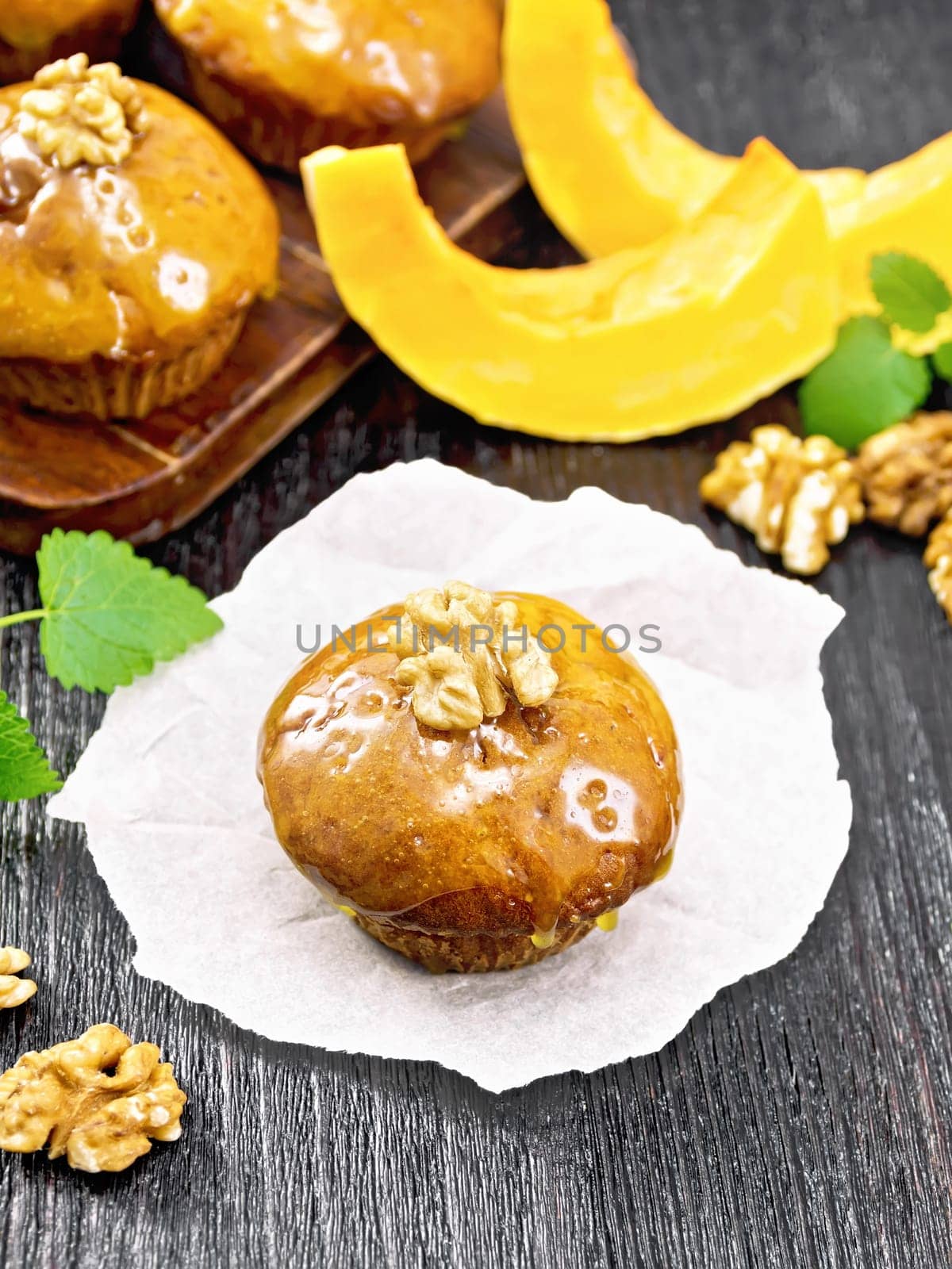 Small pumpkin cupcake with orange glaze and walnuts on paper, sprigs of mint on a dark wooden board background