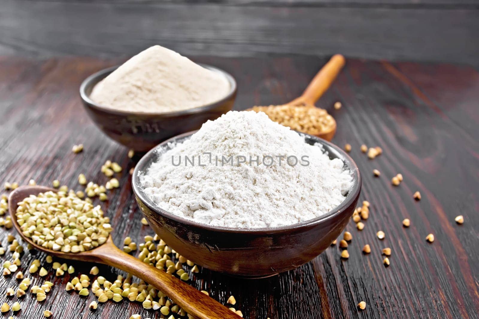 Buckwheat flour from green and brown cereals in two bowls, groats in spoons and on the table against the background of a dark wooden board