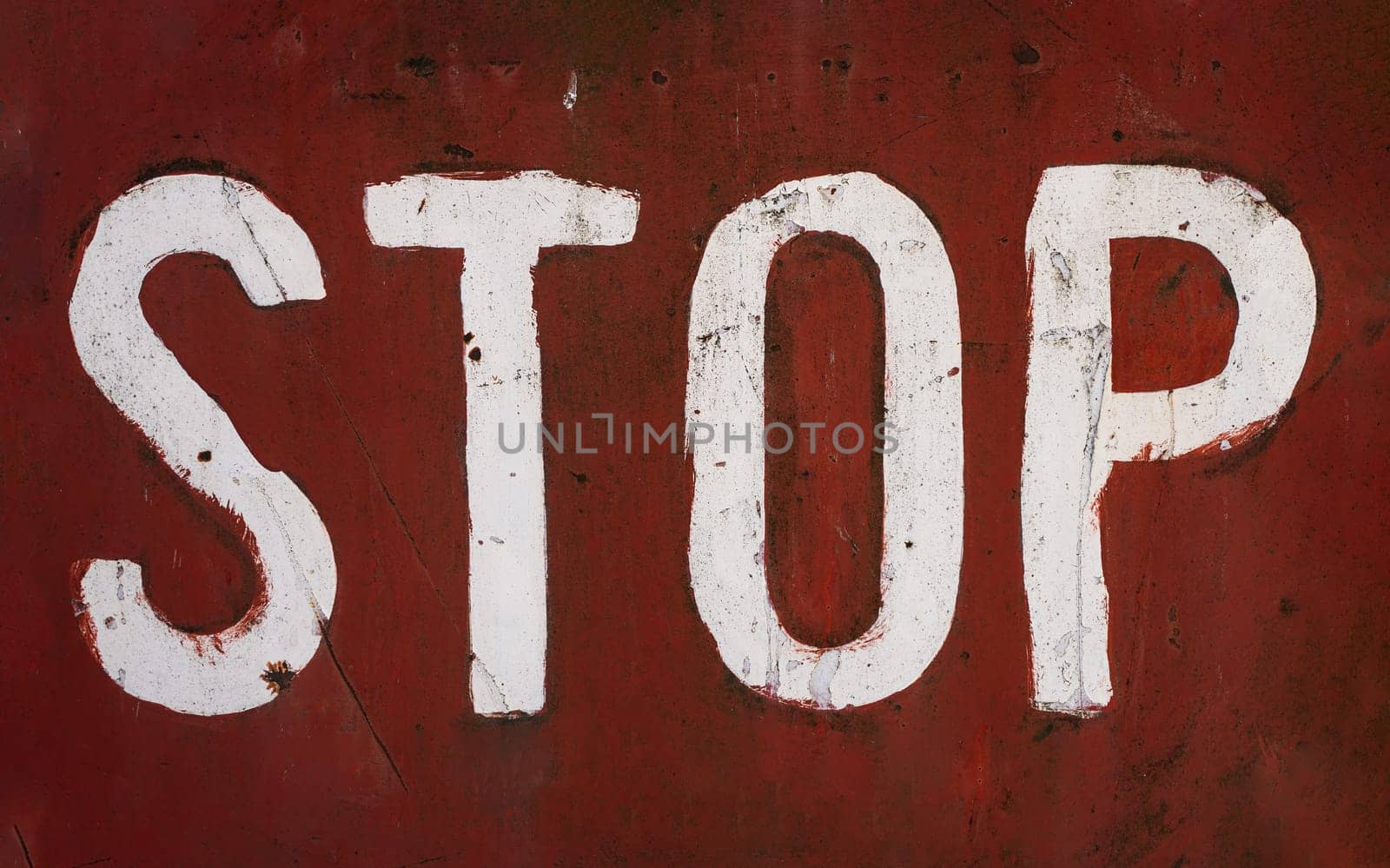 front view closeup of word stop written with white paint and capital letters brush typeface style on red rusted metallic plate texture