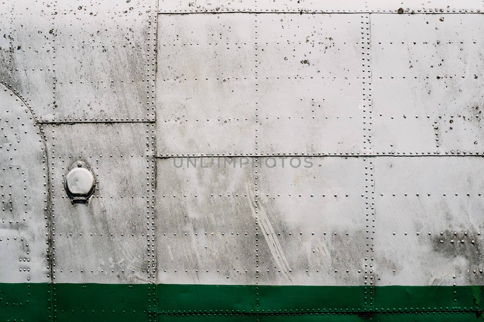 front view closeup of old airplane metallic hull fuselage plating with rows of bolts and rivets industrial texture