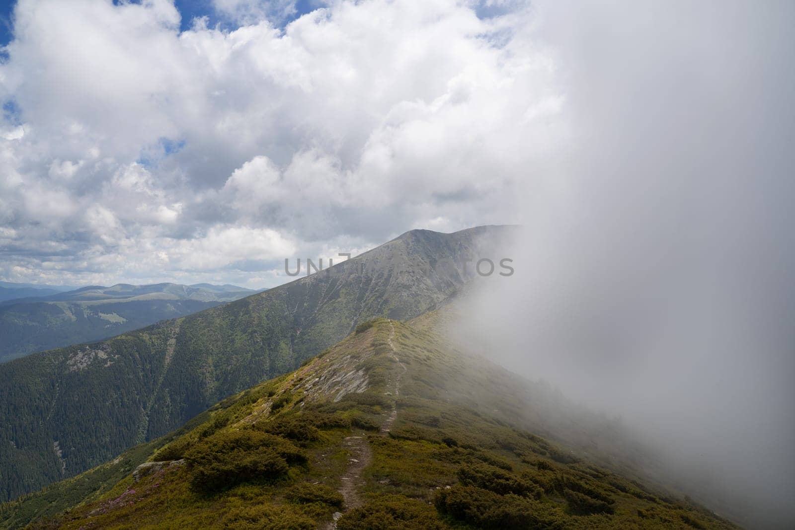 landscape with green mountain peak with cloud mist passing by and trail going on down the ridge