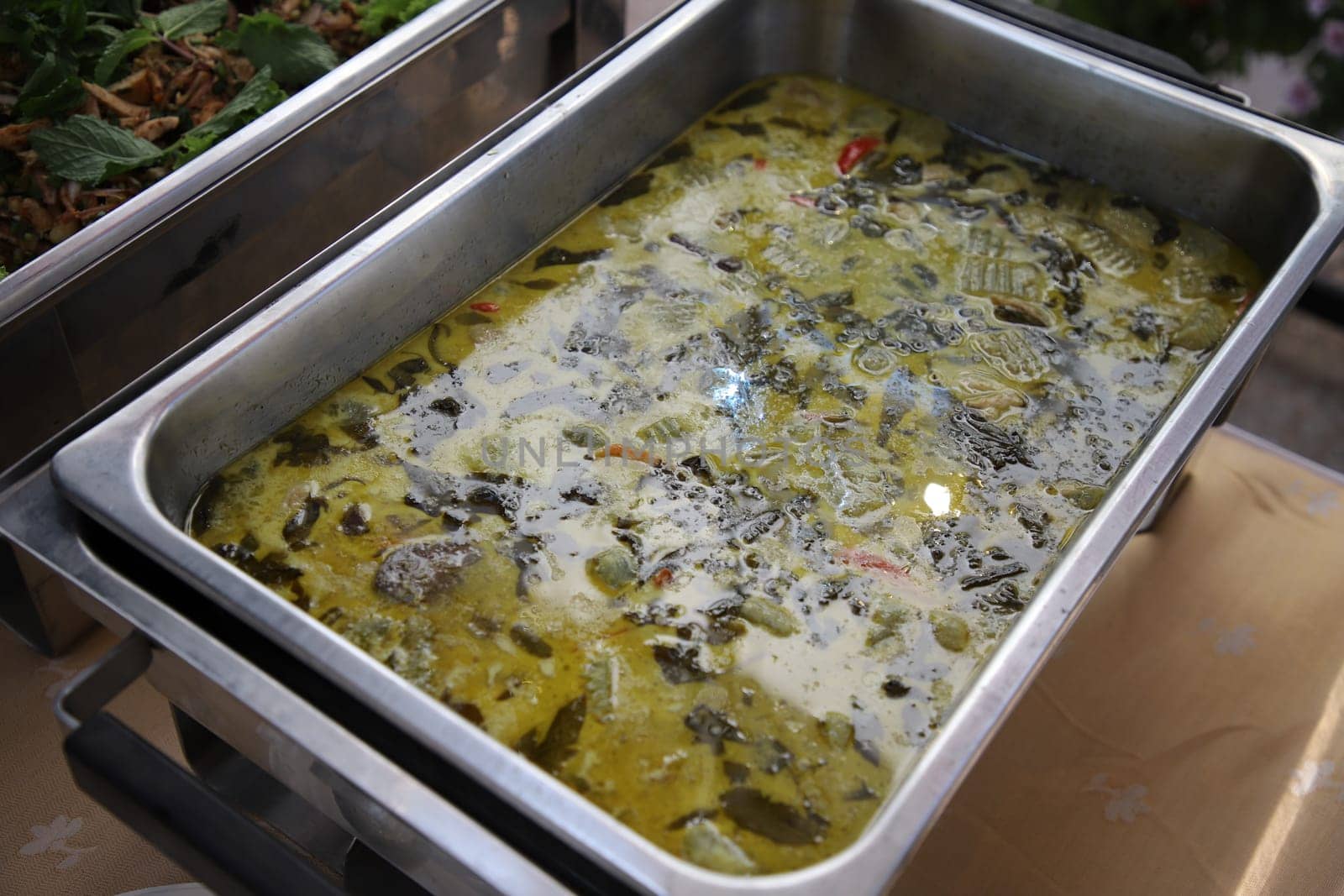 Thai food, Chicken Green Curry in buffet line. The container is a rectangular stainless steel tray. Selective focus.