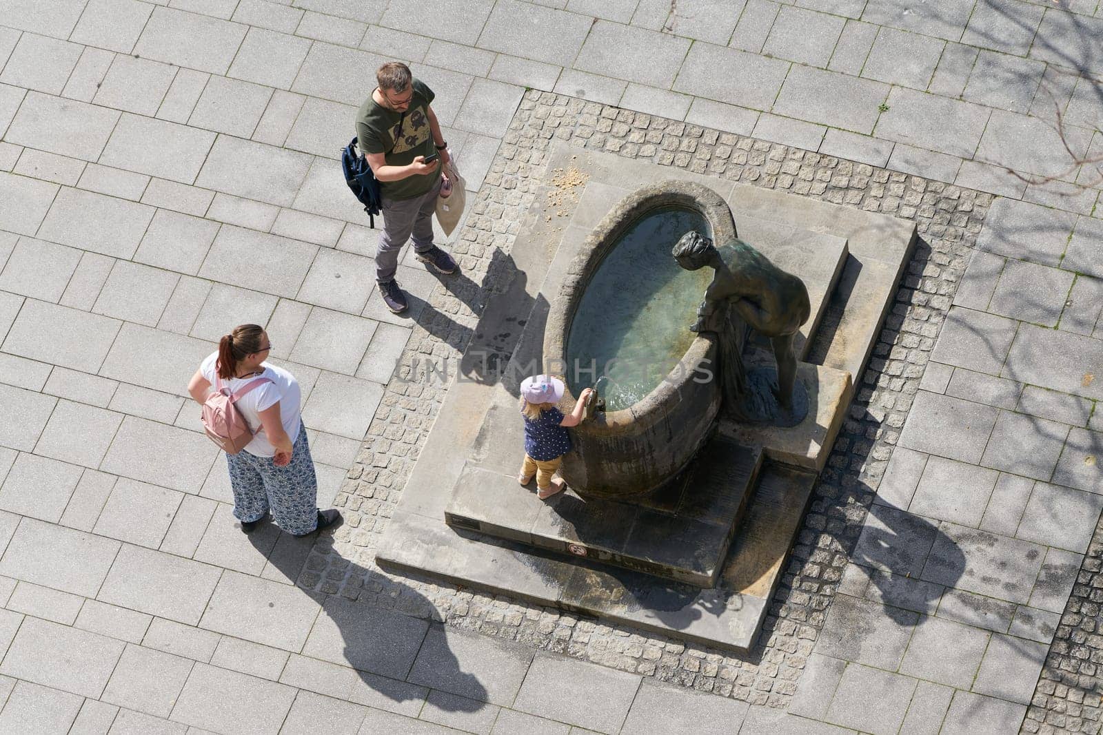 Family with child seeks cooling at a fountain in the summer in the city center of Magdeburg in Germany