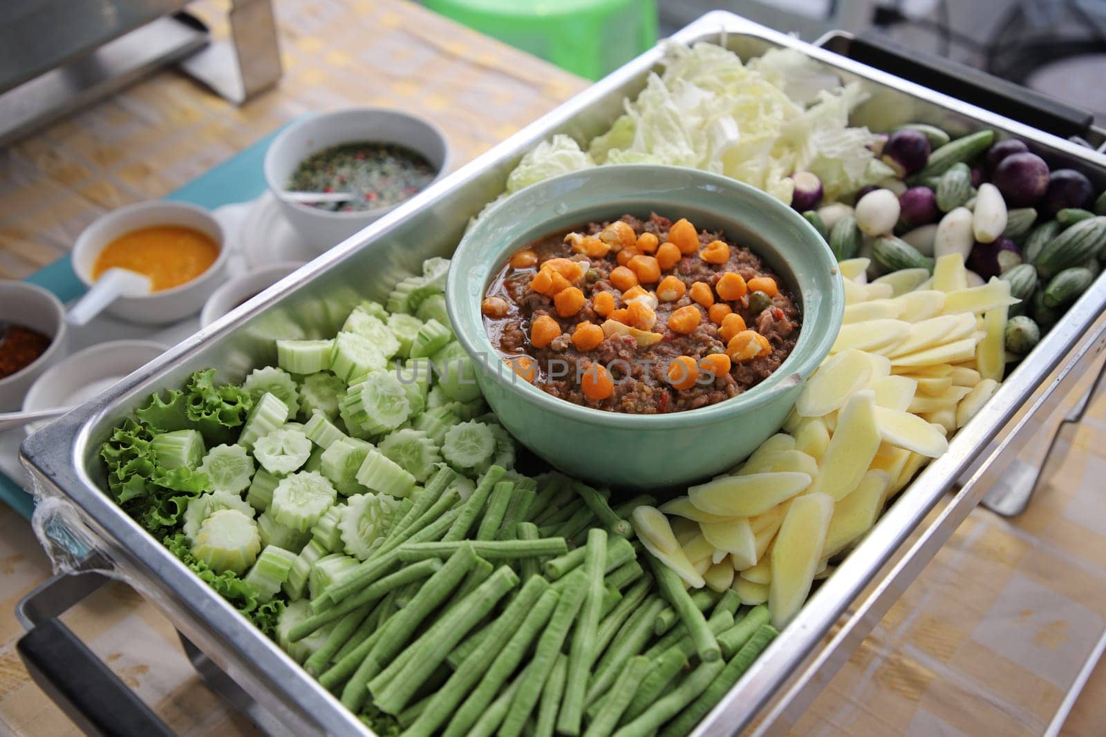 Thai food, Nam Prik Kai Poo (Crab’s Roe Chilli Dip) with many kinds of vegetables in buffet line. The container is a rectangular stainless steel tray. Selective focus.