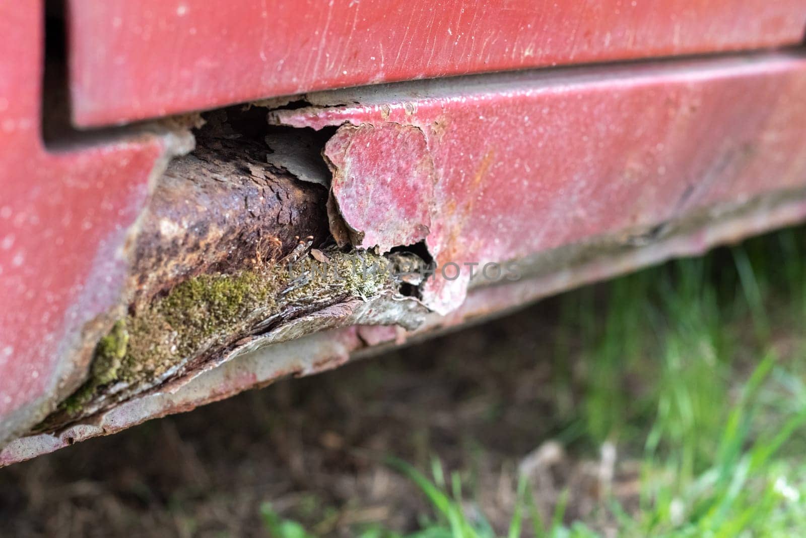 Rusty driver's door sills. Corrosion of the body of a red old car after winter. Influence of reagents in winter on an unprotected vehicle body. Damage to the left side, rotten threshold on the bottom