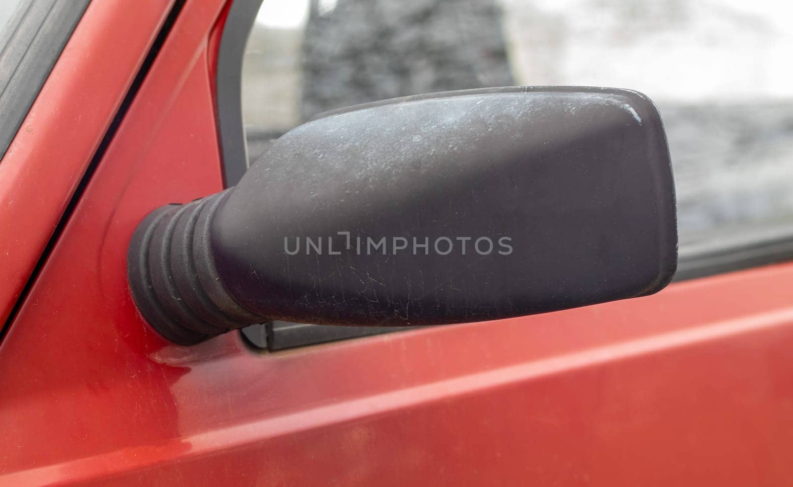 Side left black plastic rearview mirror on a red car. Exterior side view mirror on the driver's side on an old car