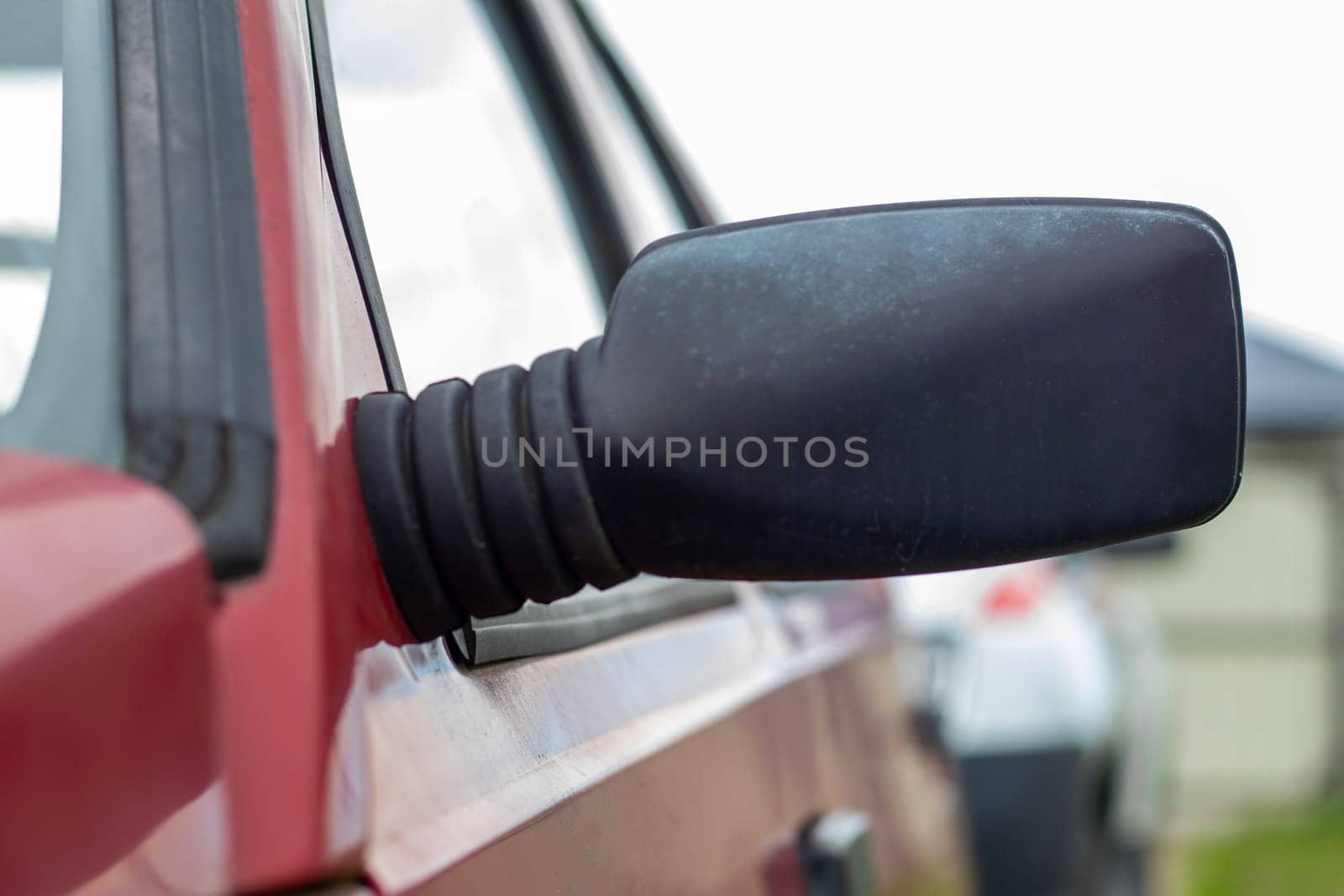 Side left black plastic rearview mirror on a red car. Exterior side view mirror on the driver's side on an old car