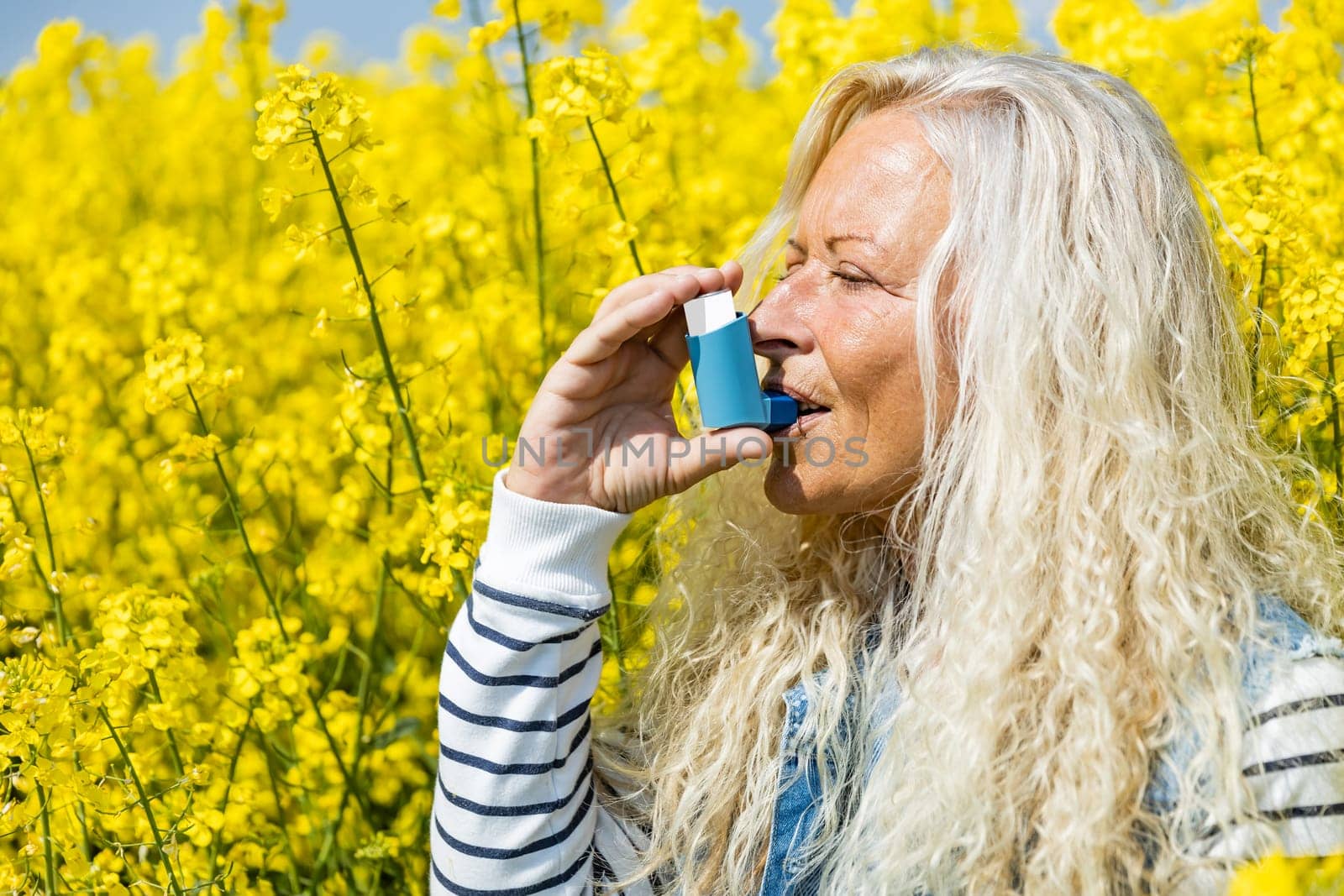 Woman with inhaler having asthma attack on spring day near a rapeseed field