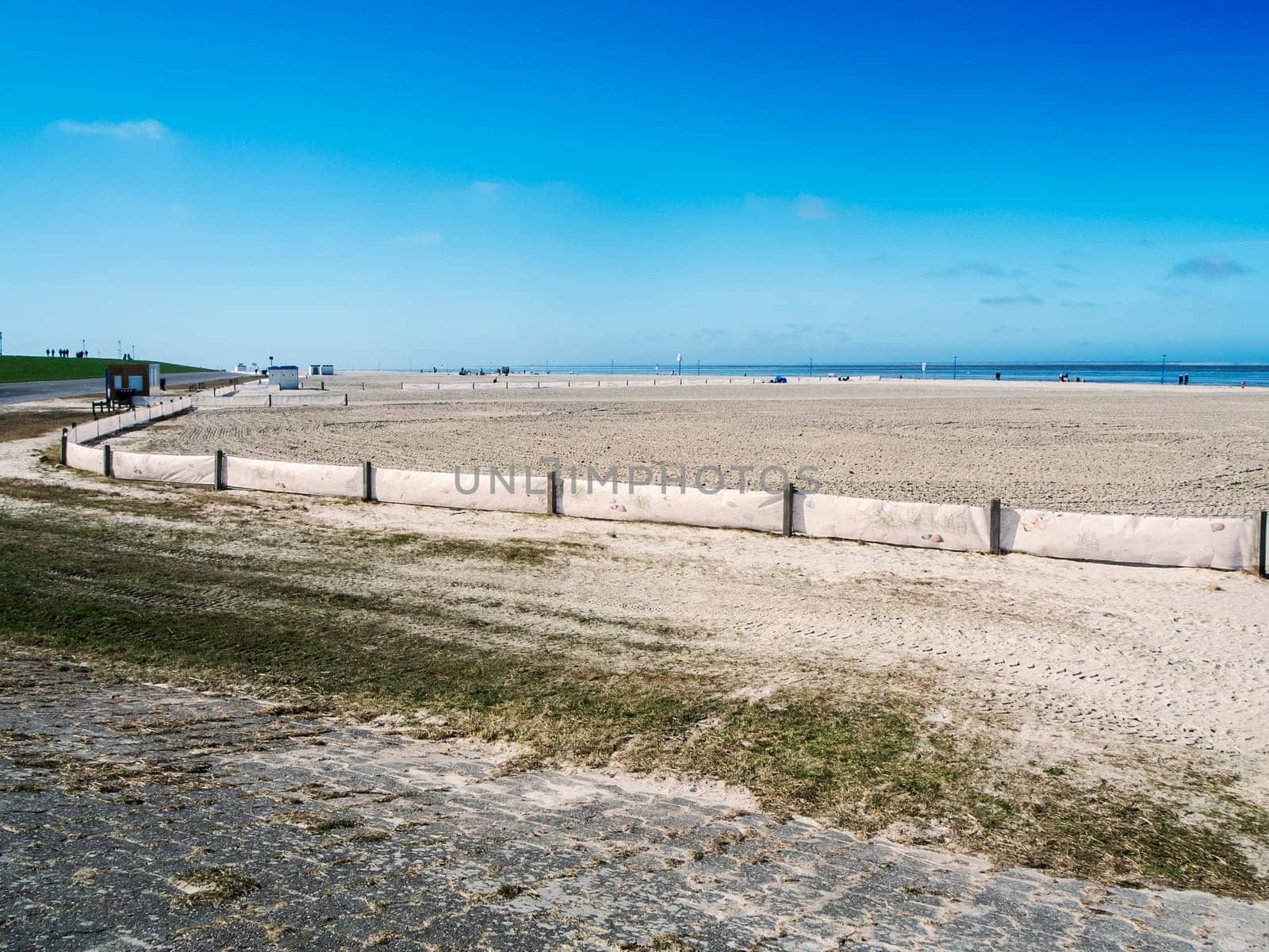 Landscape view of the smoothed bathing beach with fence near Neuharlingersiel in East Friesland in March 2022 with a blue sky and a view to the horizon.