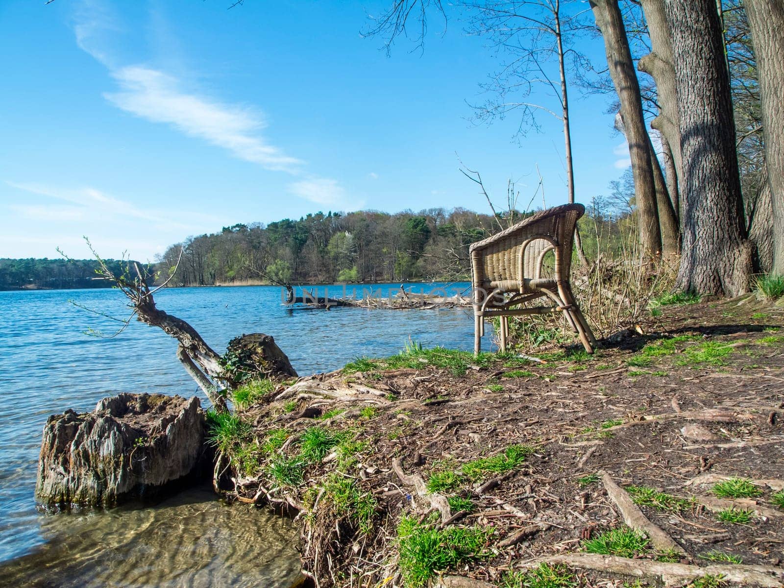 Wicker chair on the shore of the Flakensee near Wolterddorf in Brandenburg in a blue sky with veil clouds in April 2022.