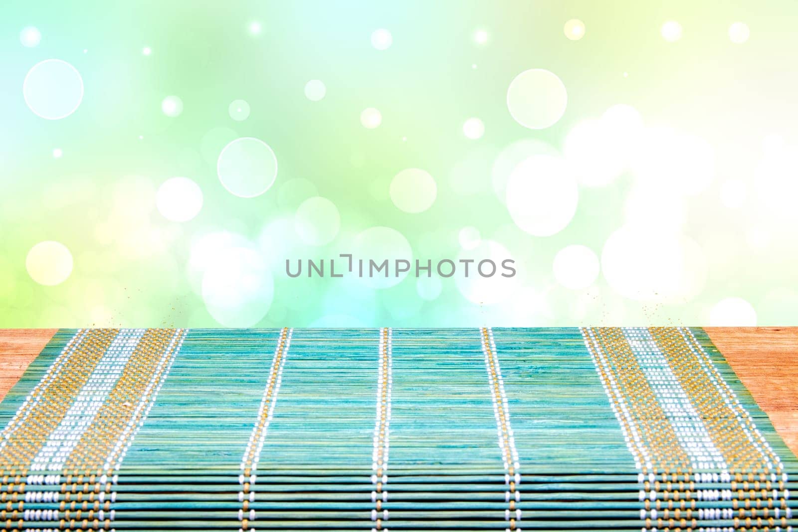 A green yellow bamboo mat on a rustic wooden table over bright blurred abstract background. Template for your product display montage. Space for design.