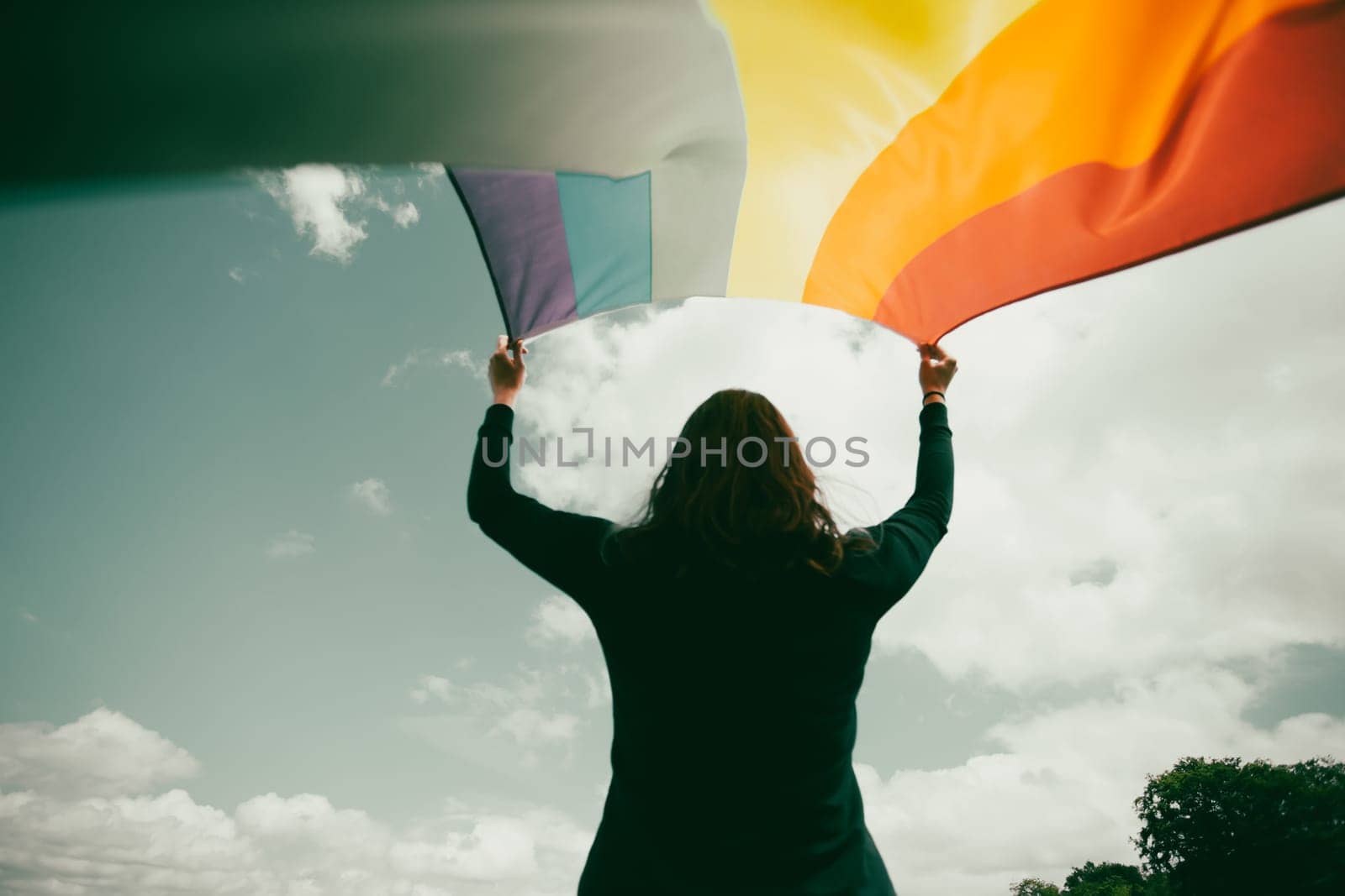 Woman sitting in a green meadow holding a Gay Rainbow Flag. Bisexual,gay, lesbian, transsexual symbol. Happiness, freedom and love concept for same sex couples