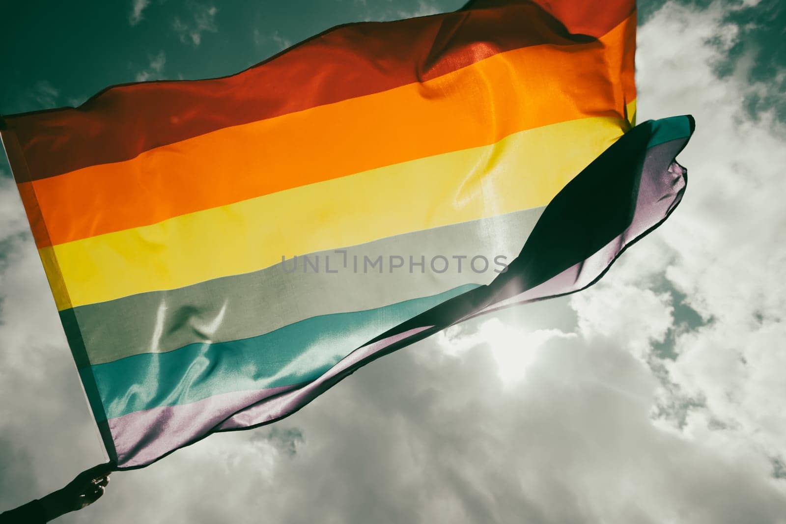 Bright rainbow LGBT flag fluttering against blue sky. LGBT community, happiness, freedom and love concept for same sex couples.