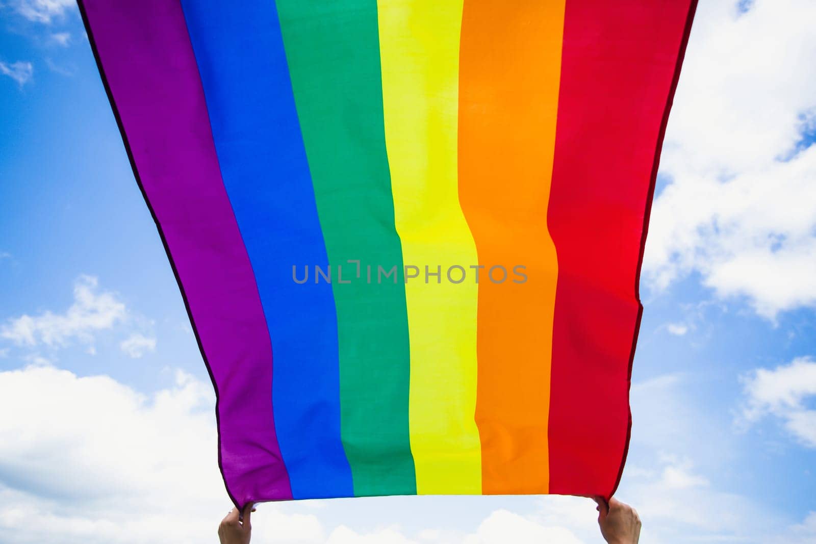 Bright rainbow LGBT flag fluttering against blue sky. LGBT community, happiness, freedom and love concept for same sex couples.