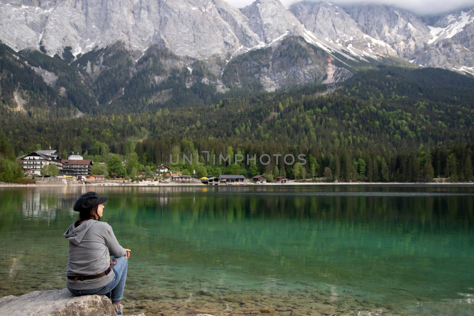 Tourist sitting on a rock and watching a beautiful view over lake Eibsee in the Bavarian Alps. Famous touristic destination in Europe