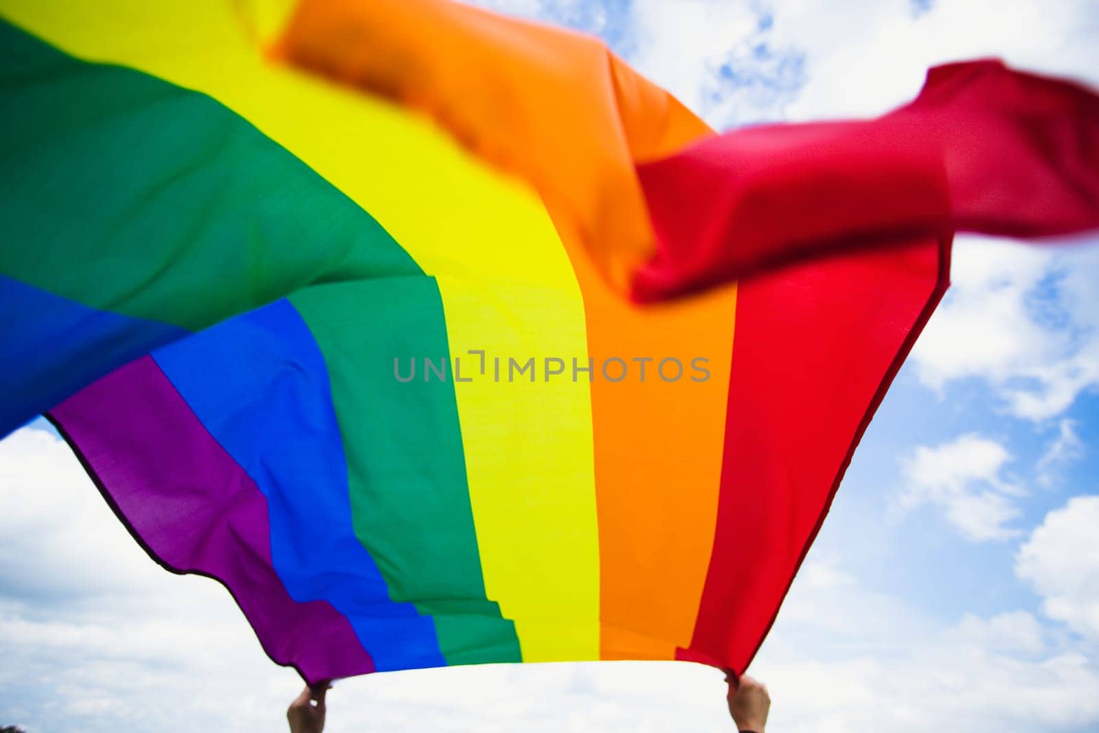 Bright rainbow LGBT flag fluttering against blue sky. LGBT community, happiness, freedom and love concept for same sex couples.