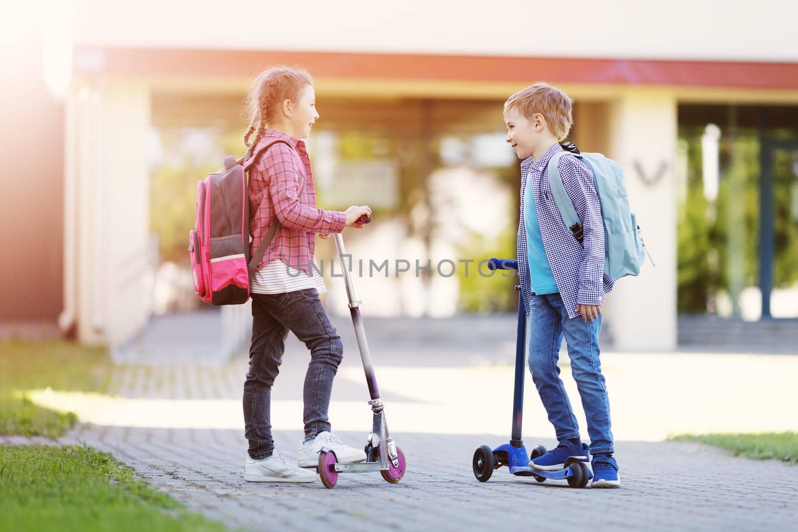 Girl and boy standing with scooters at school and talking together. Concept of back to school and friendship.