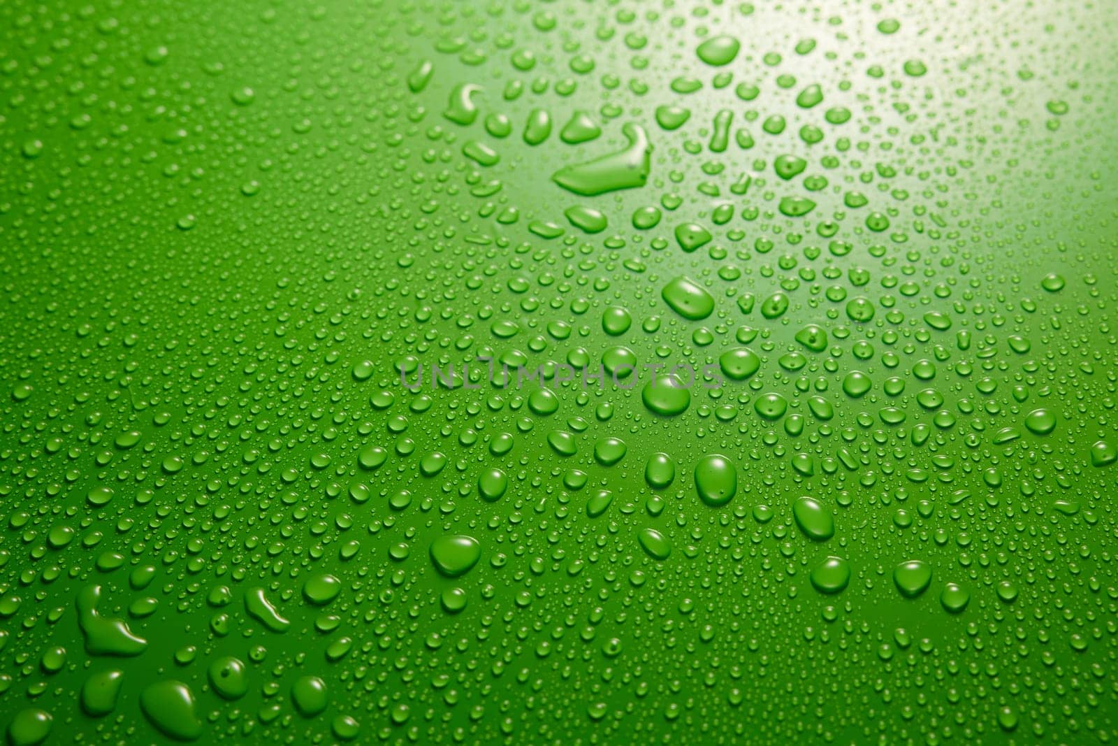 Full frame of clean green background covered with various drops of water flowing down in light room during rainy weather