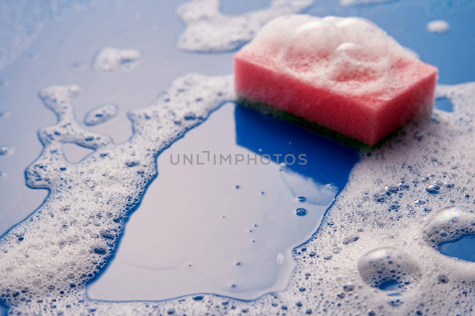 From above of wash scrub sponge with foam placed on wet blue background with soap during household routine in light room