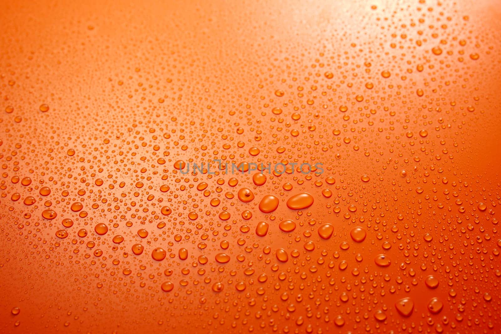 Full frame of wet clear orange background with condense and clear small round water drops flowing down in light room