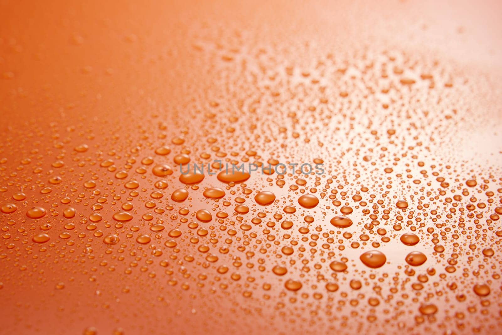 Full frame of clean orange background covered with various drops of transparent liquid with small round shapes in light room