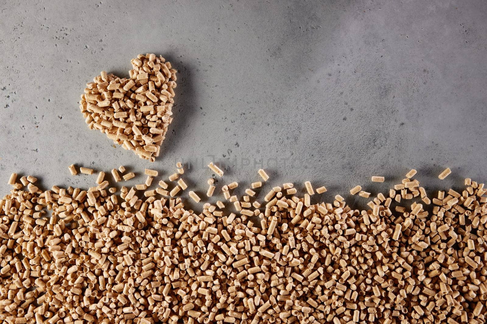 Top view of pile of solid fuel pellets scattered on gray background and forming heart