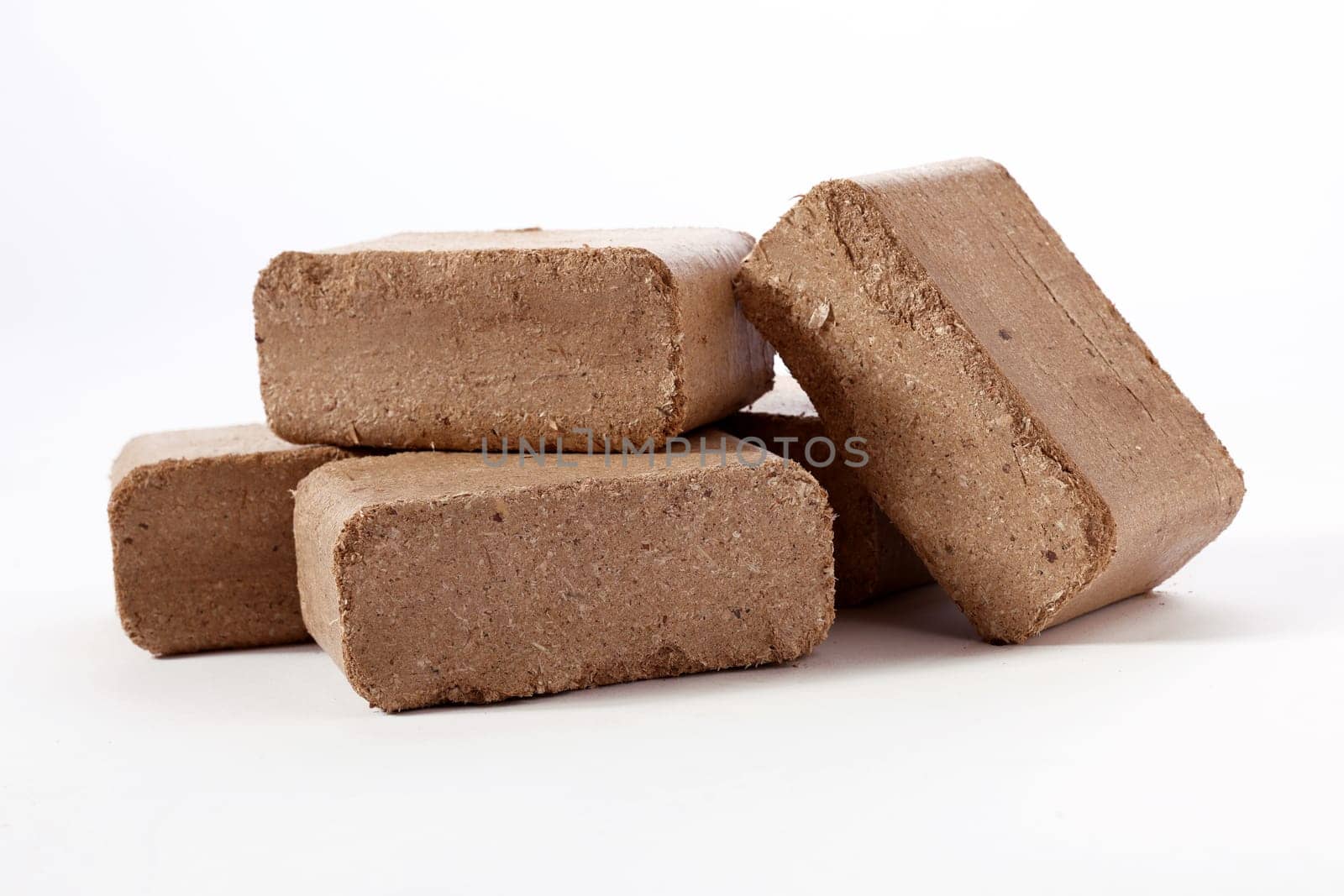 Pile of brown compressed peat biomass briquettes placed on each other on white surface in studio