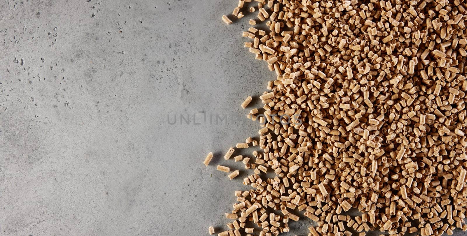 Top view of heap of natural brown fuel pellets scattered on gray concrete table