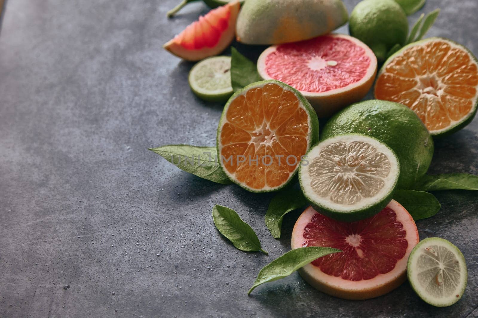 From above of various halved citrus fruits with lime and grapefruit placed on gray background with leaves in light room