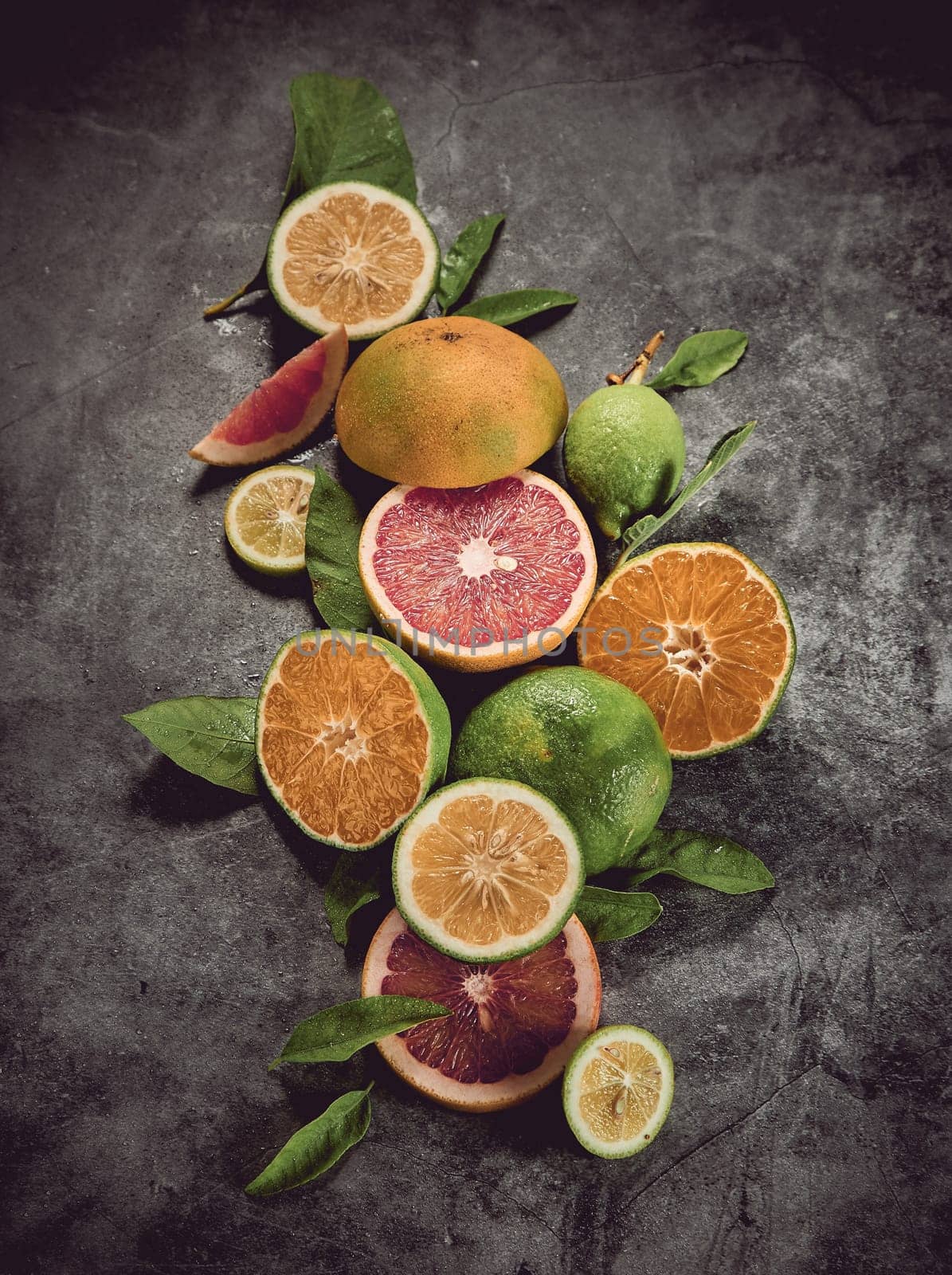 From above of various colorful citrus fruits with grapefruits and limes served on gray background with leaves in light studio