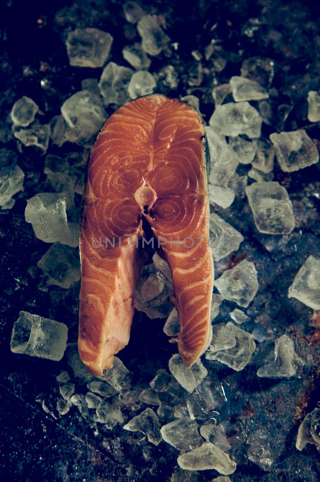 Top view of uncooked steal of red salmon served on table with ice cubes in light kitchen during cooking process