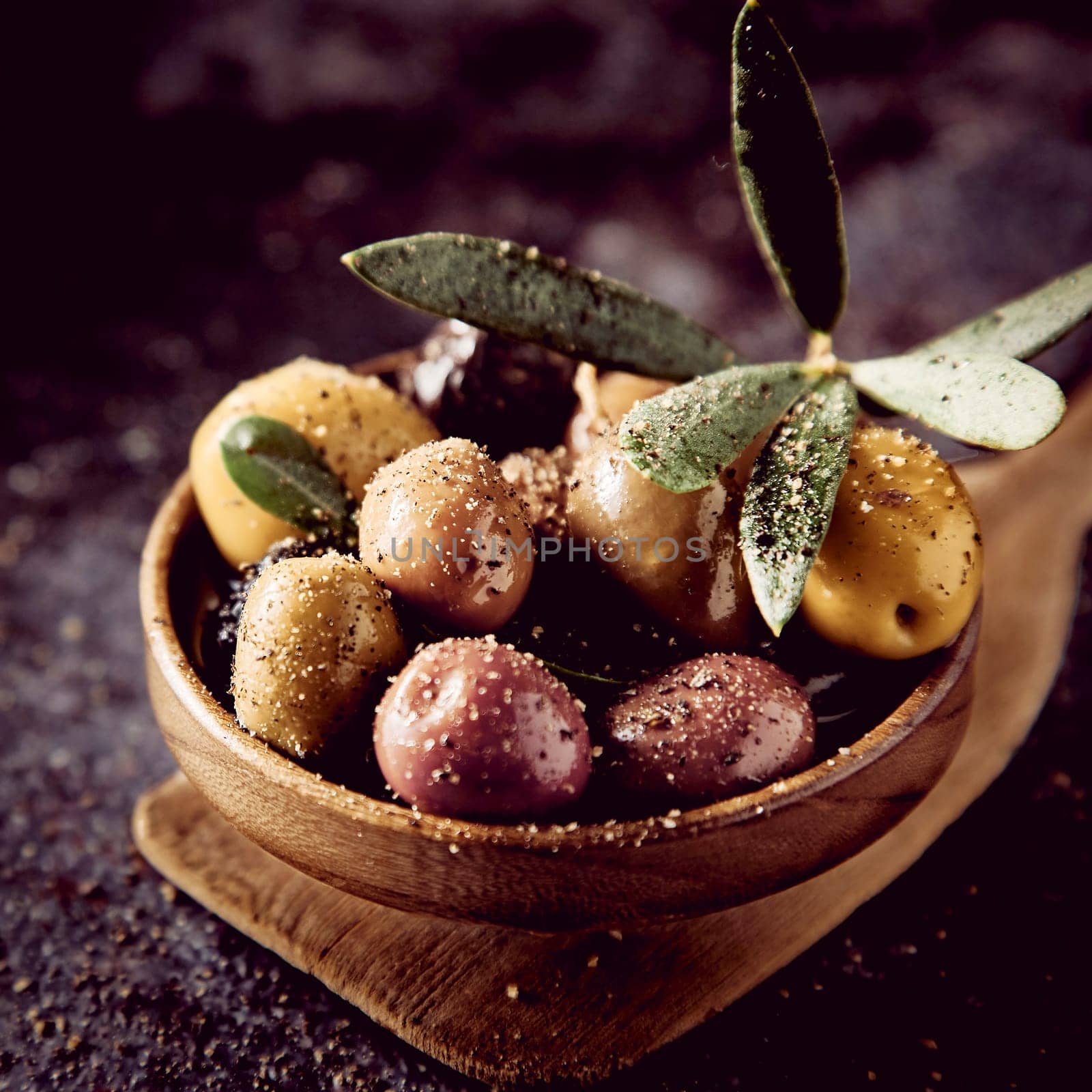 Bunch of assorted types of delicious pickled olives with seasoning and green leaves served on wooden spatula in light kitchen