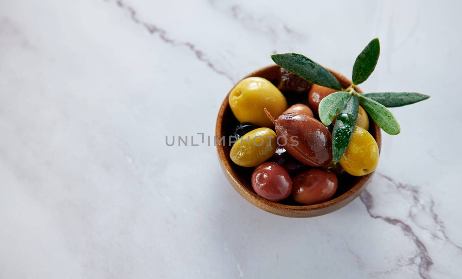 From above of tasty fresh different types of ripe marinated olives with green leaves served in bowl on white background