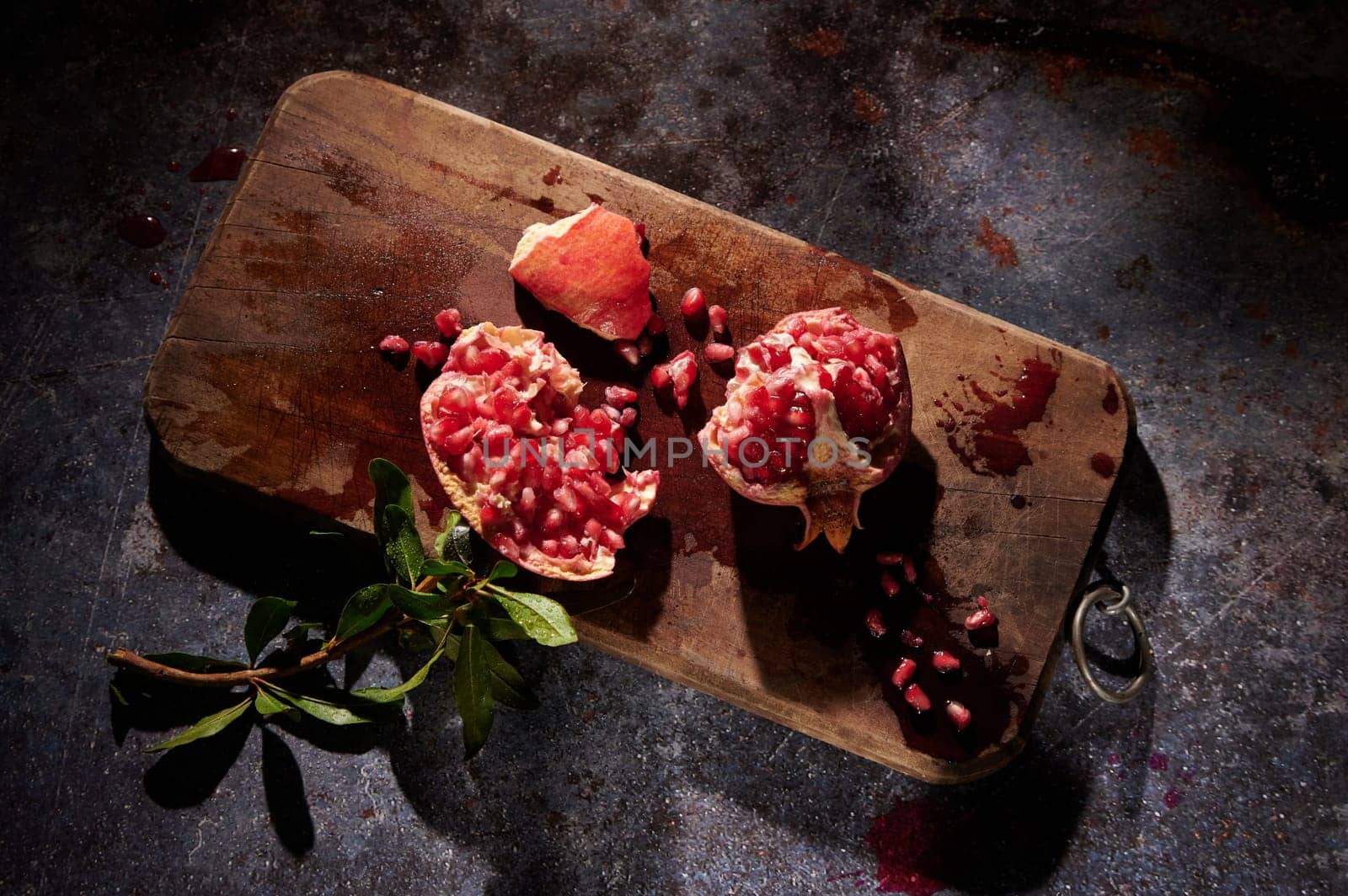 From above pieces of ripe red pomegranate with seeds placed on wooden chopping board on gray background in light kitchen