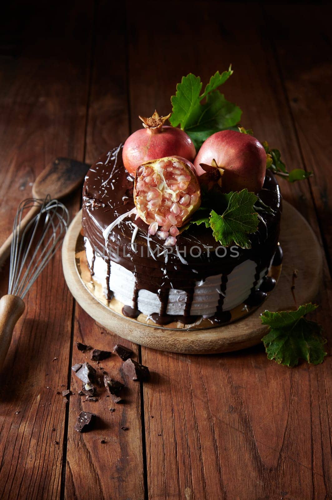 From above of delicious decorated cake made of figs and pomegranate with chocolate smudges served on wooden table with utensils