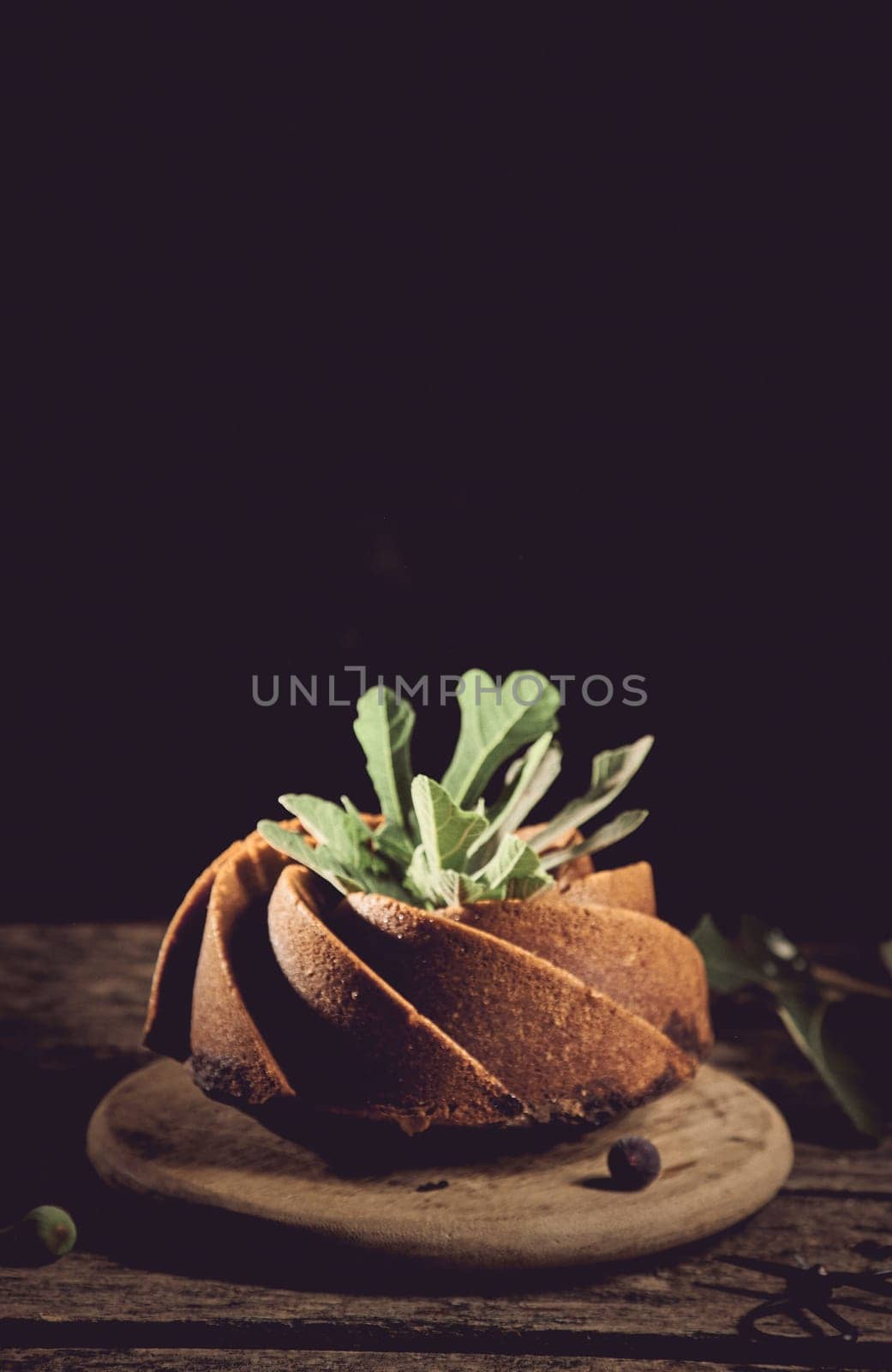 Delicious freshly baked cake made of fig decorated with green leaves served on wooden board against black background in kitchen