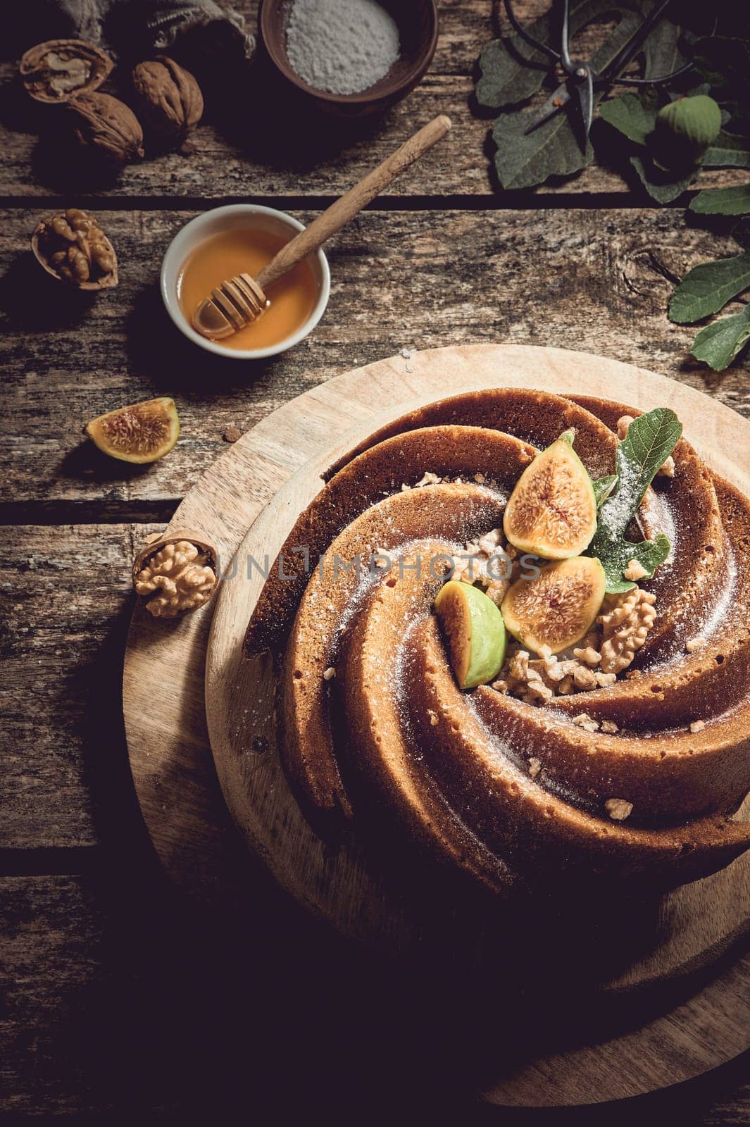 From above of sweet freshly baked fig cake served on wooden cutting board near walnuts and honey in light kitchen