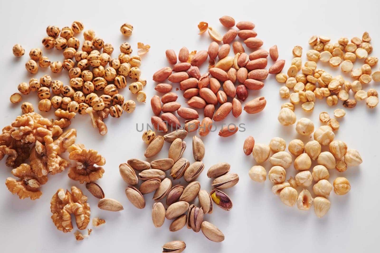 From above piles of pistachio and hazelnut placed near walnuts and peanuts on clear white background in modern light studio