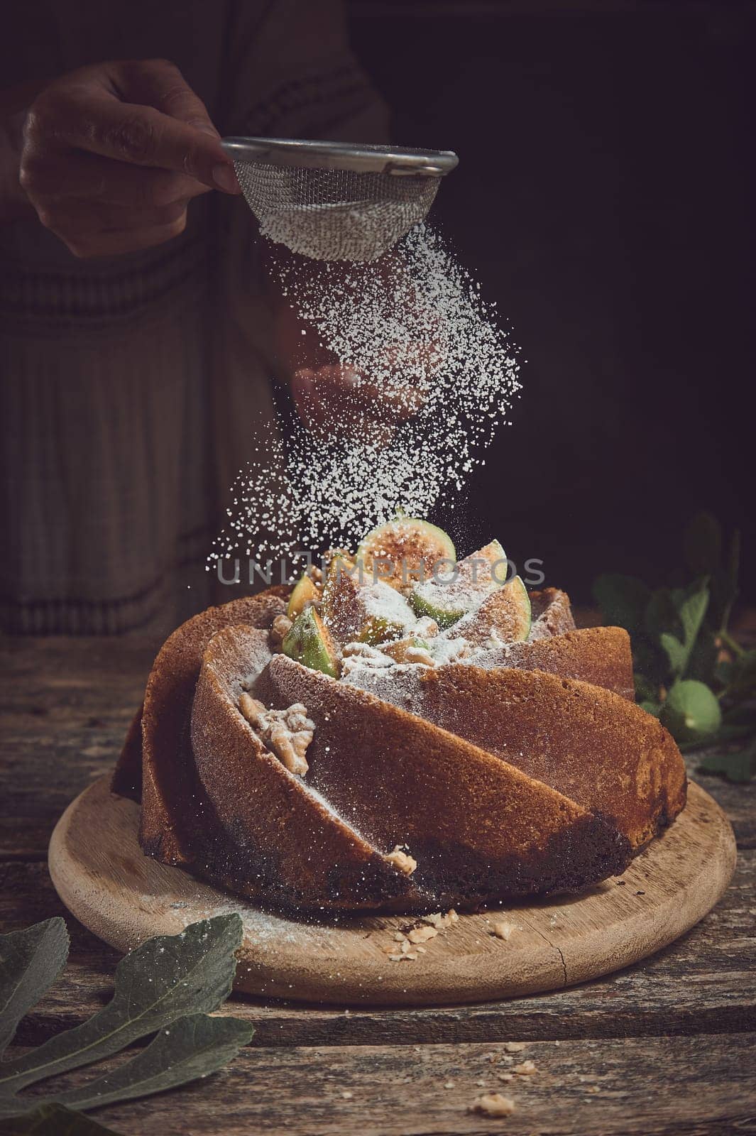 Crop anonymous cook sifting powdered sugar through sieve on sweet homemade fig cake served on cutting board in light kitchen