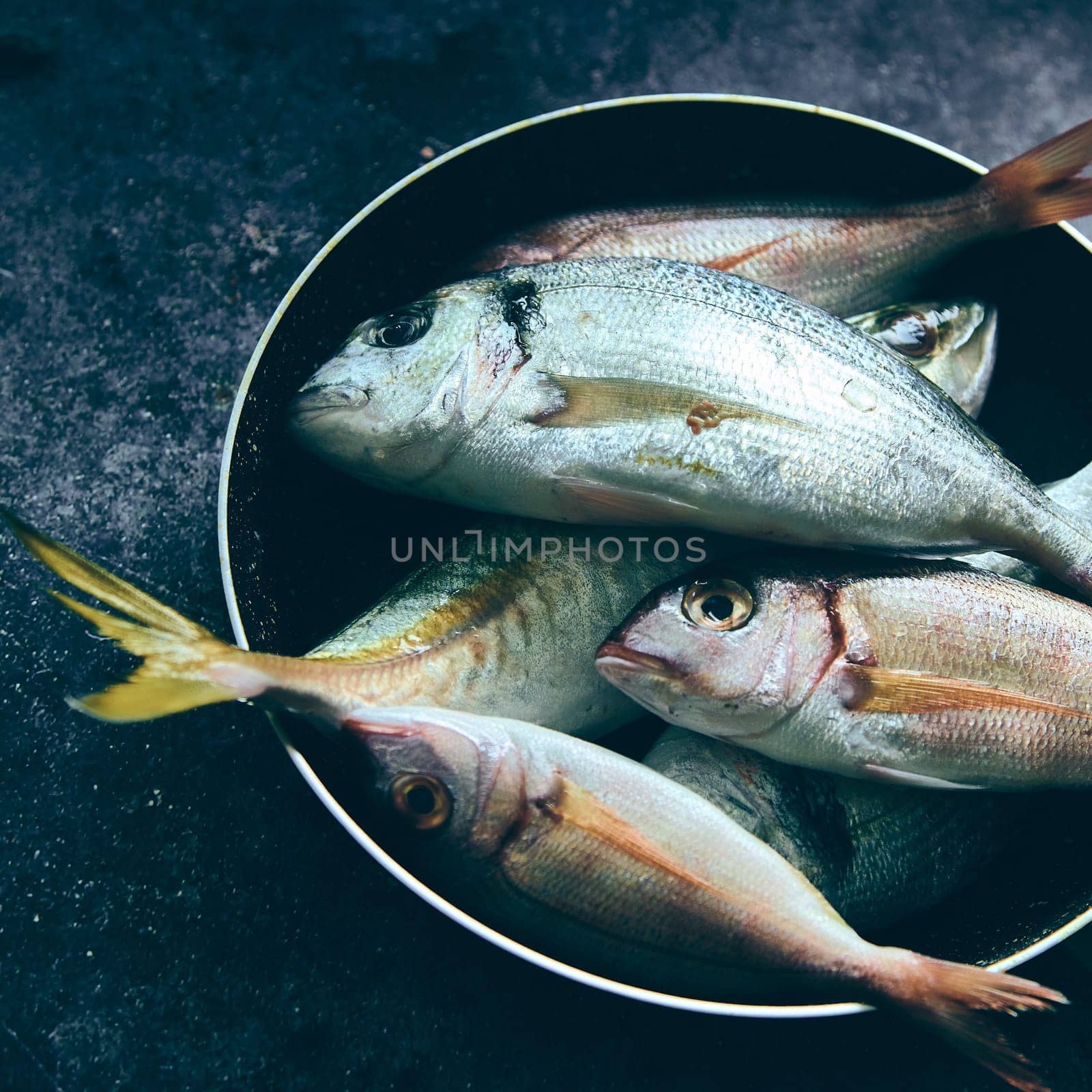 From above stack of raw tasty fish placed in metal pot on gray background in light room during cooking preparation