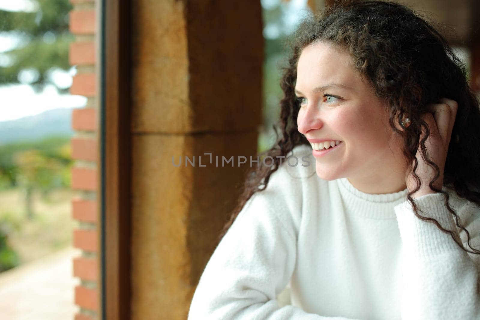 Happy female looks through a window sitting in a house interior