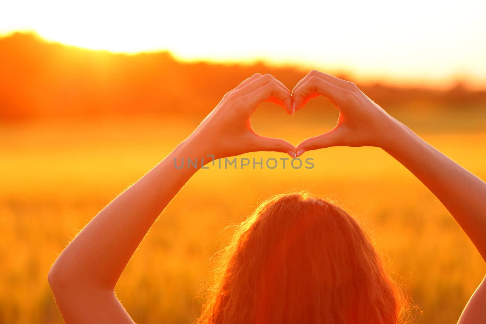 Close up of a woman doing heart shape in a field at sunset