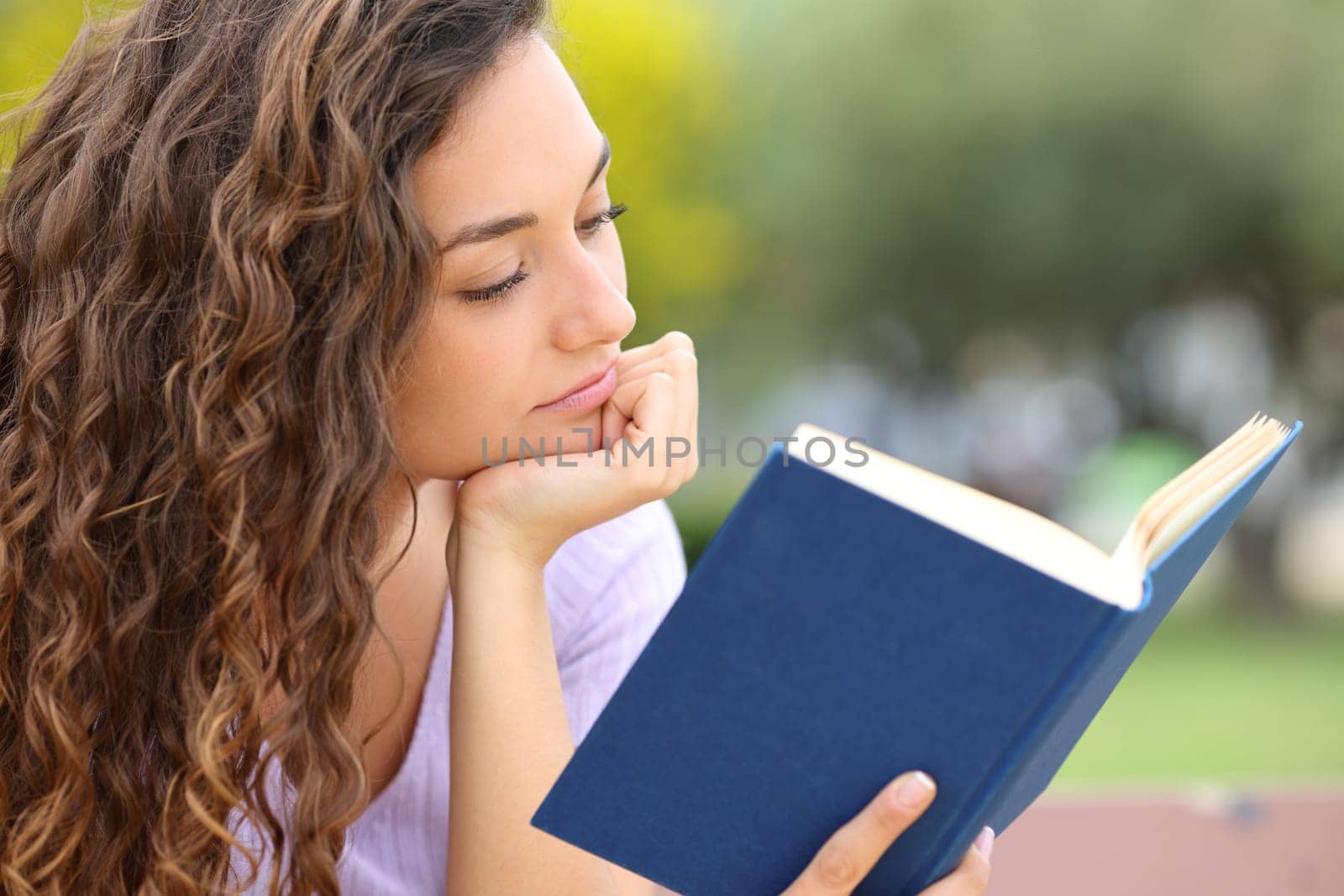 Relaxed woman reading a book sitting in a park alone