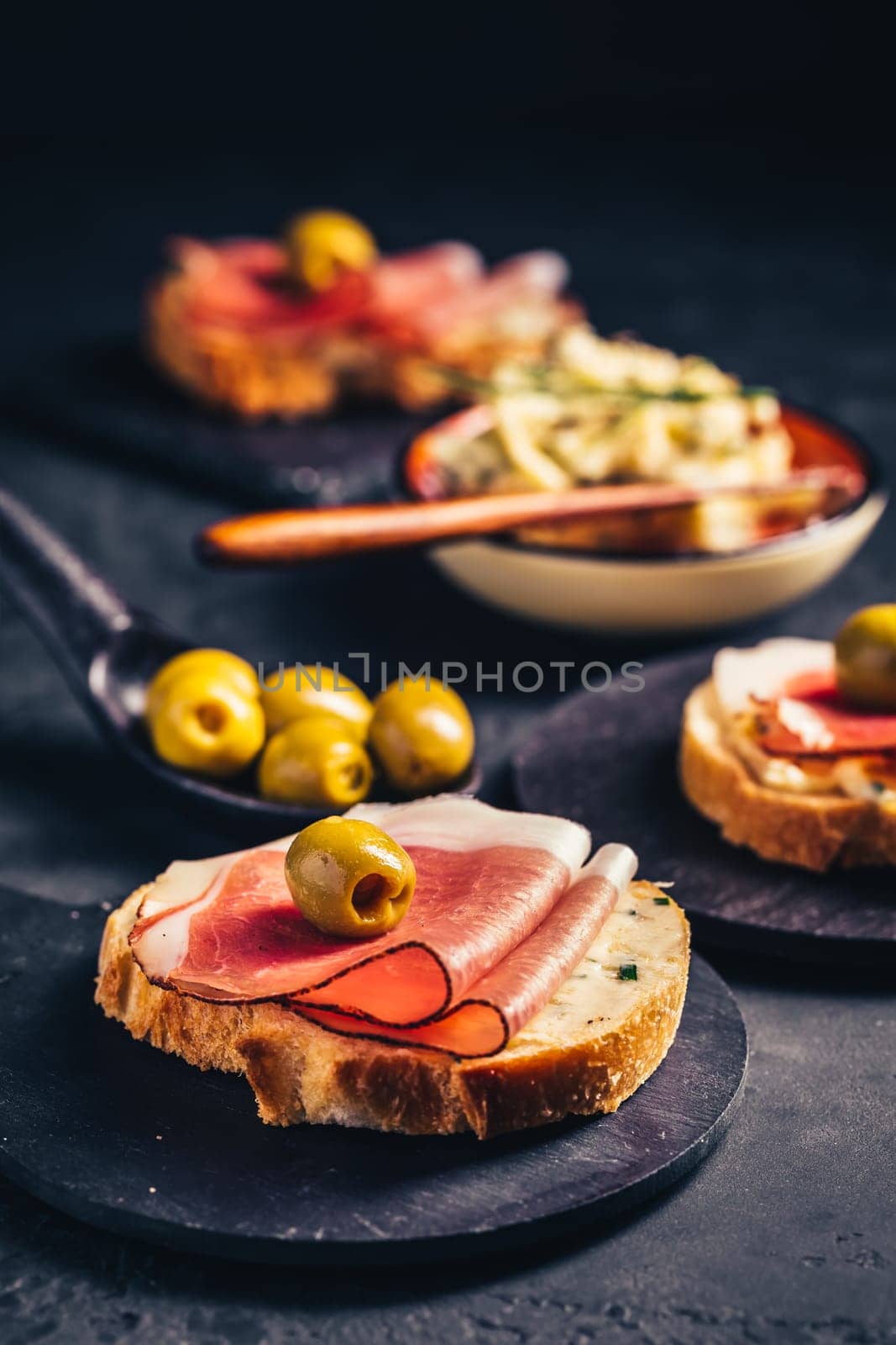 Roasted bread or open sandwich with garlic butter spread and serano ham and olive on dark background